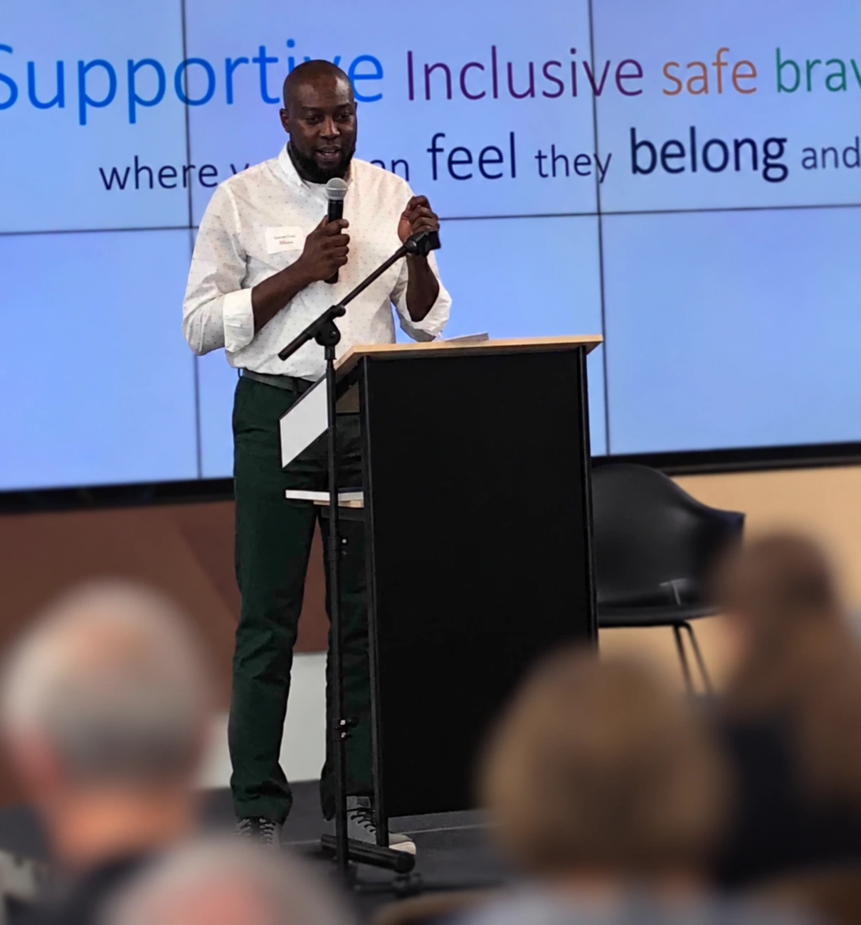 Dauda Raji speaking at a community gathering, with other attendees blurred